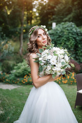 A cute curly woman in a white wedding dress with a wedding bouquet and wreath in her hair standing back to the camera in nature. Concept escaped bride. Forward to a happy bright future Runaway