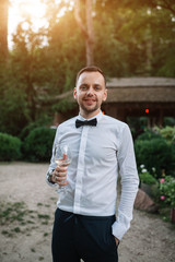 a handsome man in a white shirt and tie is tasting white wine from a transparent glass. Concept business dinner. Outdoor portrait