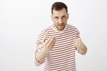 Fototapeta premium Your face pisses me off. Portrait of outraged angry adult male, showing come here gesture and raising fist, looking from under forehead with threatening look, wanting to fight or punch offender