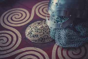 Fototapeta premium Scandinavian, viking helmet with chain mail on a red shield with golden shapes of sun, weapons for war