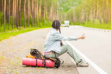 woman sitting on a backpack and  hitchhiking on the road