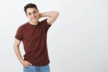 Shy good-looking masculine guy in red t-shirt, touching back of neck and holding hand in pocket,...