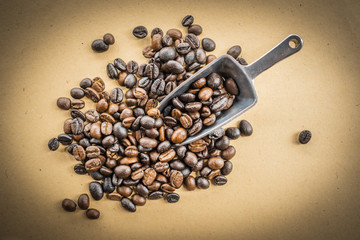 macro of coffee beans with metal scoop on rustic paper background