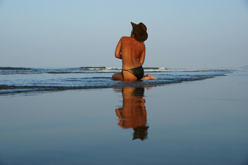 Lonely girlon blue sky background and blue water reflection, the girl in a leather hat is reflected in the water