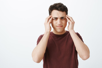 Naklejka premium Nie można skupić się na pracy z powodu bólu głowy. Portret ponurego, nieostrego atrakcyjnego mężczyzny, marszczącego brwi i grymasów od bólu głowy, cierpiącego na migrenę i szukającego środków przeciwbólowych