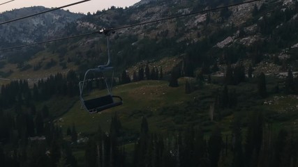 Drone shot passing by ski-lift chair over darkening mountains in Alta, Utah