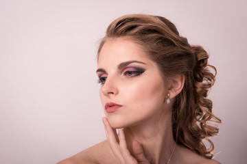 Brown-haired woman with a professional hairdress and make-up is holding hands near the face on a light background close-up.