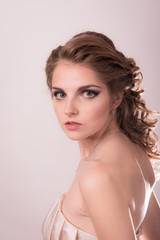 Brown-haired woman with professional hair and make-up against a light background close-up.