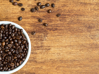 Macro shot of coffee beans on wooden background and coffee in white bowl, flat lay, copyspace