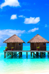 Water villas on wooden pier in turquoise ocean on the white sand beach - obrazy, fototapety, plakaty