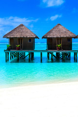 Water villas on wooden pier in turquoise ocean on the white sand beach