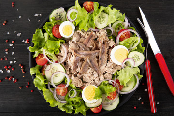 Salad with tuna, anchovies and vegetables. Mediterranean food. The background is black. Top view. Copy space. Horizontal shot.