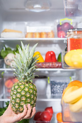 Person holding pineapple against open fridge