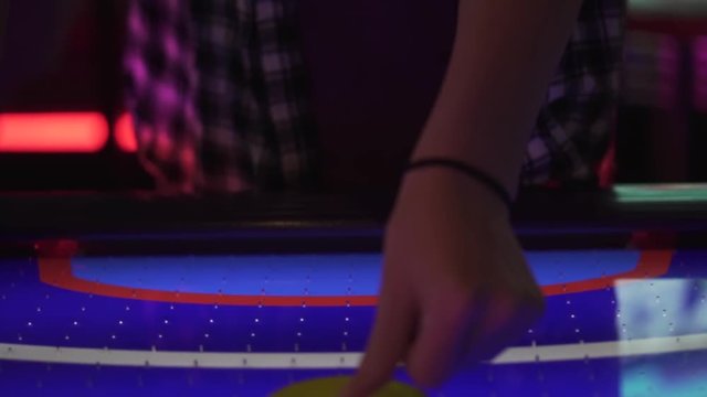 Slo-motion, front-facing shot of a girl placing an air hockey puck down and hitting it.