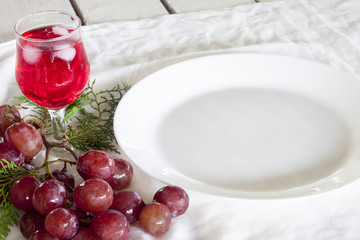 Dinner on the white table with red water in the glass , grape fruit and empty plate white color on fabric.