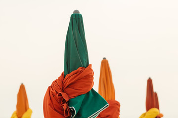 Beach umbrellas on foggy day in Deauville, fashionable holiday resort in Normandy, France. Folded colorful parasols in the morning on the empty beach. Leisure and seaside vacations concept. Close up