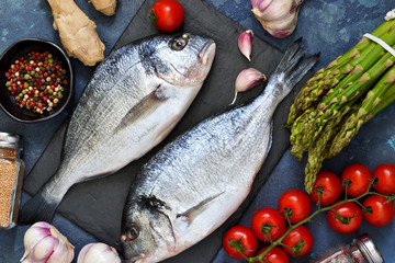Fresh, raw Dorado fish with asparagus, tomatoes and spices on a concrete background. Ingredients for cooking.