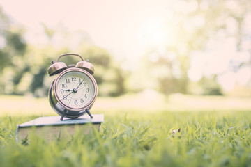 alarm clock on book in park, time for learning and reading concept