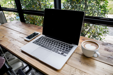 Side view laptop with mobile phone and a cup of fresh coffee latte art on wooden table.