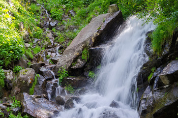 small waterfall in the mountains against the background of green trees