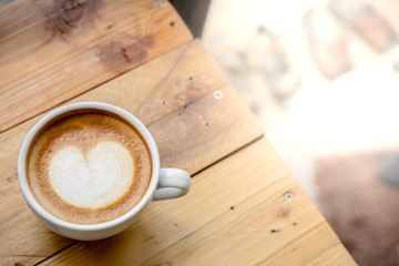 Top view of Latte hot coffee in a cup with latte art on wooden table background and warm light.