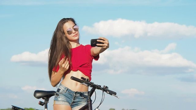 A beautiful girl takes pictures of herself. A girl with a bicycle takes a picture of herself on the phone.