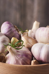 Close-up view of a lot of fresh raw garlic bulbs with tiny rosemary leaves in wooden bowl
