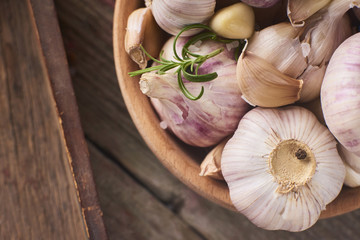 Close-up view of a lot of fresh raw garlic bulbs with tiny rosemary leaves in wooden bowl