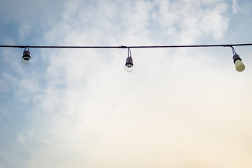 Obraz premium Vintage light bulbs hanging on a cable, decorated for outdoor party.