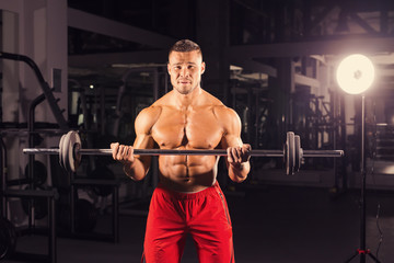 Fototapeta na wymiar Handsome power athletic man with barbell. Strong bodybuilder with six pack, perfect abs, shoulders, biceps, triceps and chest
