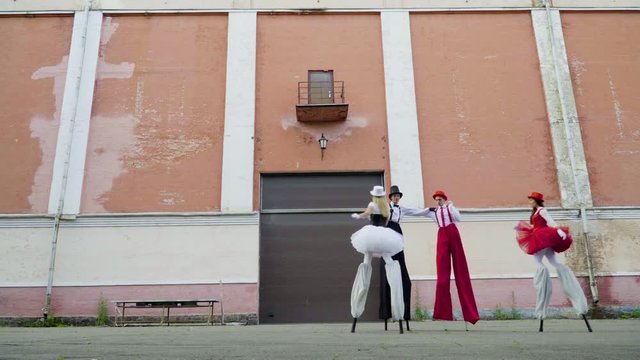 Two comic couples on stilts are dancing near the building