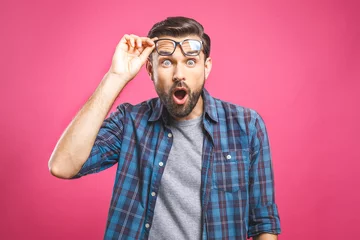 Foto op Plexiglas OMG! It's incredible! Portrait of handsome young man in glasses looking at camera while standing against pink background. Close up portrait of bearded man keeping his mouth open. © denis_vermenko