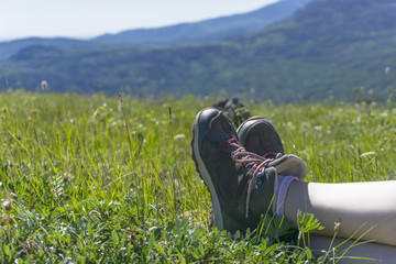 legs in trekking boots of a woman resting lying on the grass of the alpine meadow in the mountains