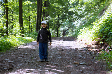 Obraz premium Portrait of cheerful caucasian little boy in summer with big blurry background, scene on a trip in the woods.