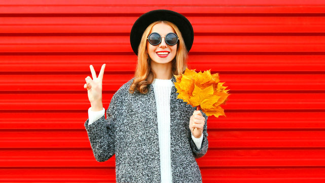 Happy pretty autumn cool girl with yellow maple leaves on a red background