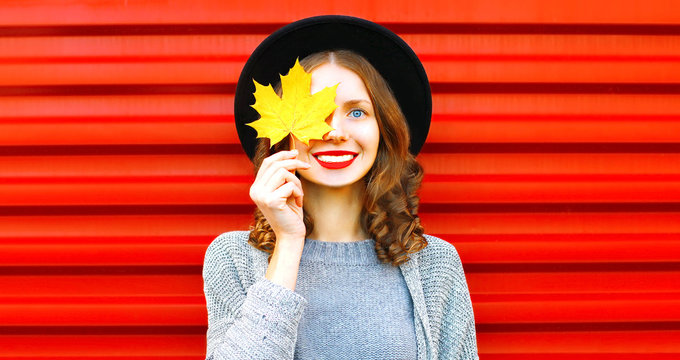 Happy cool girl  hides one eye yellow maple leaf on a red background