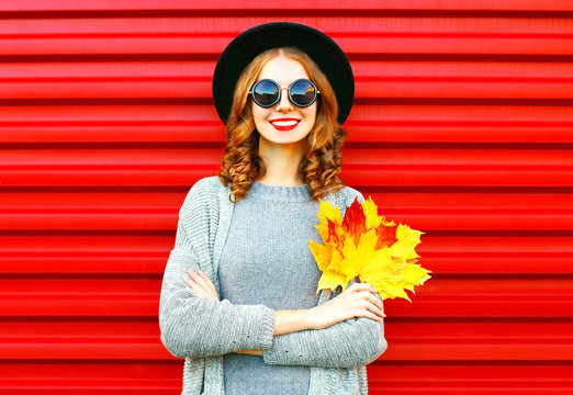 Stylish autumn woman holds yellow maple leaves on a red background