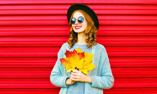 Stylish happy portrait smiling woman with yellow maple leaves on a red background