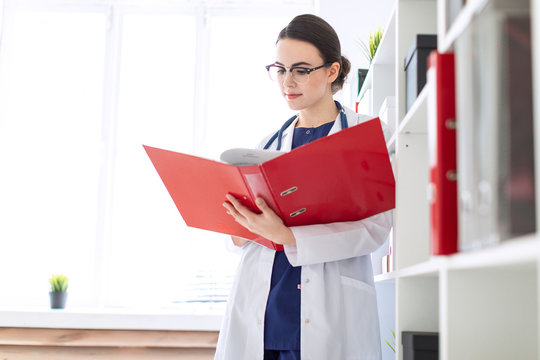 A beautiful young girl in a white robe is standing near the shelter and flips through a red folder with documents.
