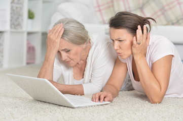 Mother and her adult daughter lying on floor and using laptop