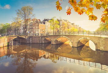 Fototapeta premium Houses and arches of bridge over canal with mirror reflections, Amsterdam at autumn, Netherlands