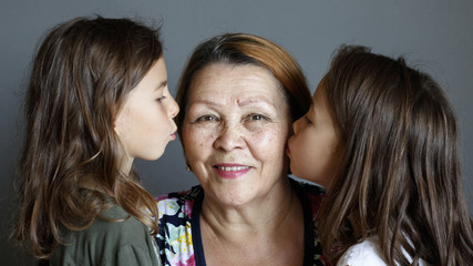 Little beautiful granddaughters kiss their beloved grandmother on both sides