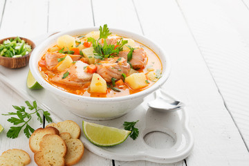 Salmon soup with cream, potatoes, carrots and parsley on white background.