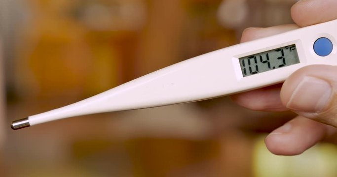 Hand holding a digital thermometer displaying 104.3 degrees fahrenheit - closeup