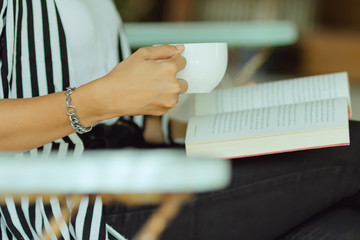 Close up of female reading book and drinking coffee in coffee shop.