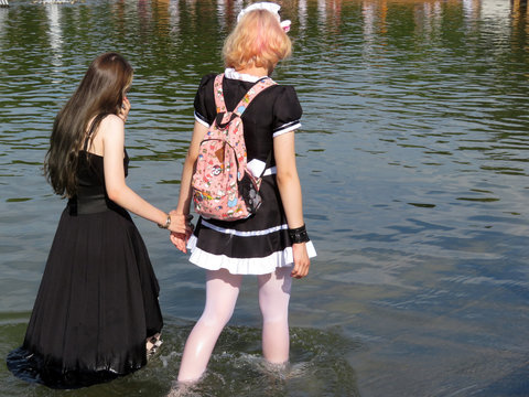 Two girls in anime cosplay walking in the water holding each other's hands. Characters of the fictional world - Powered by Adobe