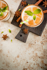 Traditional Indian drink is iced tea or chai masala, with ice cubes from chai, milk and mint leaves. With striped straws, on a wooden board. On light beige stone table. Copy space top view