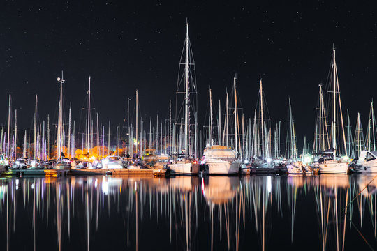Many yachts sail boats in marina bay at night mirroring in a sea - Powered by Adobe