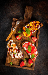 Healthy summer breakfast snack, Rye toast sandwiches with fruit and berries - strawberry, peach, banana - with chocolate sauce, dark concrete background copy space