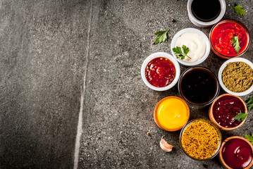 Set of different sauces - ketchup, mayonnaise, barbecue, soy, teriyaki, mustard, grain hills, pesto, adzhika, chutney, tkemali, pomegranate sauce on black stone background. Copy space top view